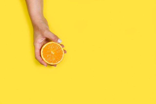 vrouw met een halve sinaasappel op een gele achtergrond met kopieerruimte - Foto, afbeelding