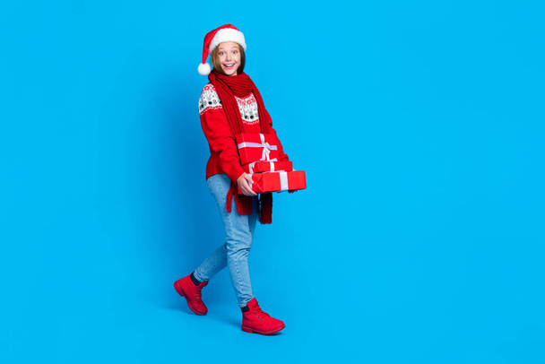 Pełna długość zdjęcie podekscytowany funky szkoła dziewczyna nosić czerwony xmas ozdoba sweter spacery gospodarstwa prezenty stos odizolowany niebieski kolor tło. - Zdjęcie, obraz