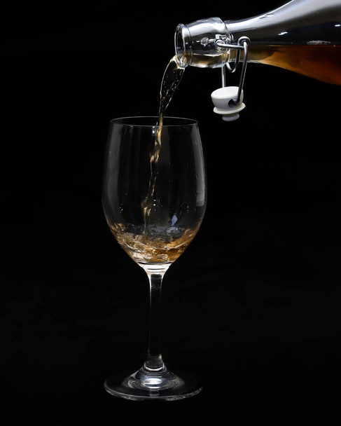 A glass and spilling wine from a bottle on a black background. Close-up - Photo, Image
