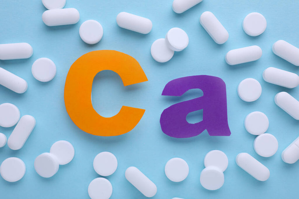 Calcium symbol made of colorful letters and white pills on light blue background, flat lay - Foto, afbeelding