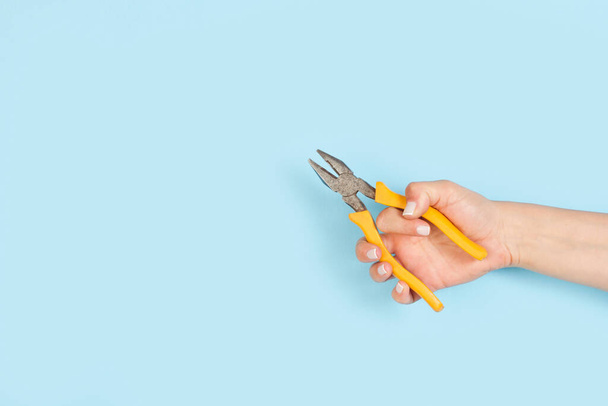 Woman hand holding a linesman pliers on a light background with copy space - Photo, Image