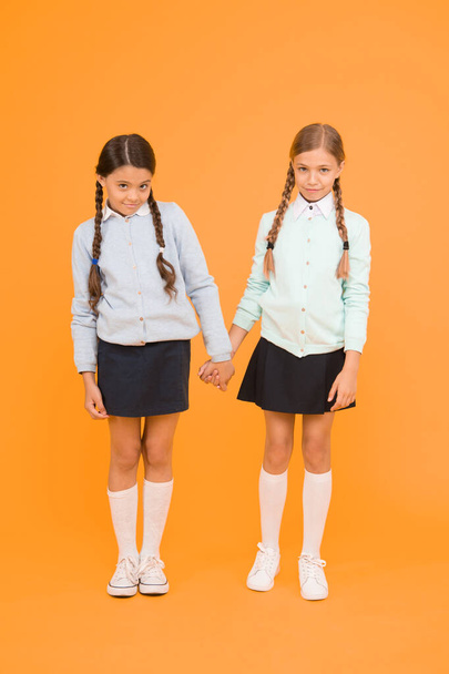 Feeling shy. Cute children holding hands on yellow background. Little children wearing school uniform. School children with fashion look. Small children with plaited hair are back to school. - Foto, afbeelding