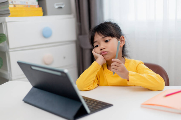 Little Asian girl sitting alone and looking out with a bored face, Preschool child laying head down on the table with sad bored with homework, spoiled child - 写真・画像