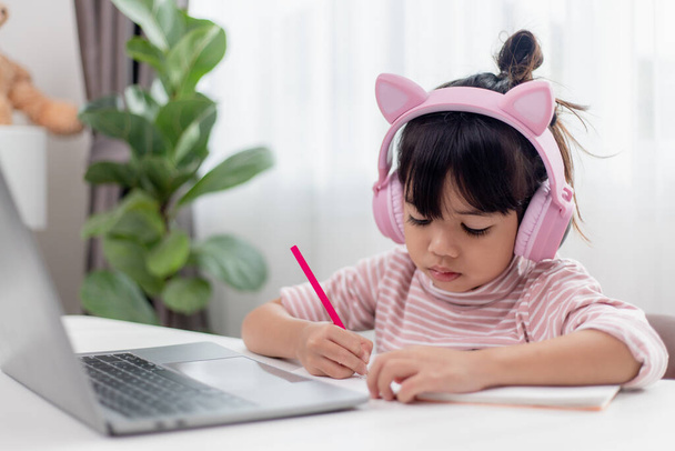 Asian little girl in headphones have video call distant class with teacher using laptop, study online on computer, homeschooling concept - Photo, Image