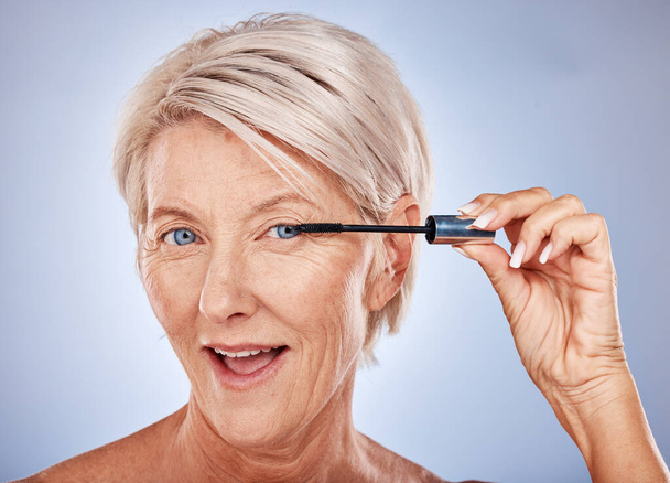 Makeup, mascara and portrait of a senior woman with a natural, cosmetic and beauty routine in a studio. Cosmetics, beautiful and elderly model with a eyelash product isolated by a gray background - Foto, Imagem