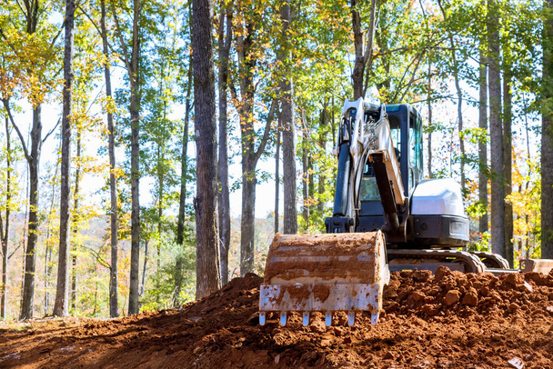 Cubo excavadora cava terreno en el sitio de construcción cerca del bosque - Foto, Imagen