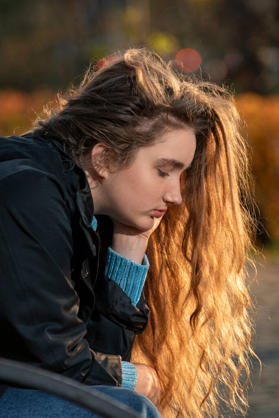 Porträt eines grübelnden netten Mädchens mit schönen langen kastanienbraunen Haaren draußen. Junge Frau mit dicken verdorbenen Haaren - Foto, Bild