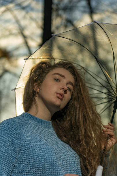 Красивая молодая женщина с коричневыми пышными непослушными волосами под прозрачным зонтиком снаружи. Осенний парк. Нижний вид - Фото, изображение