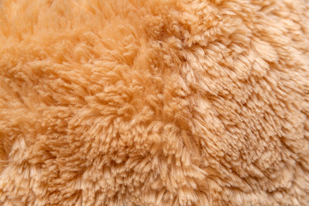 Close-up verfrommeld nepbont in perzik of beige tint. Structuur van pelsstof als achtergrond. Bovenaanzicht. - Foto, afbeelding