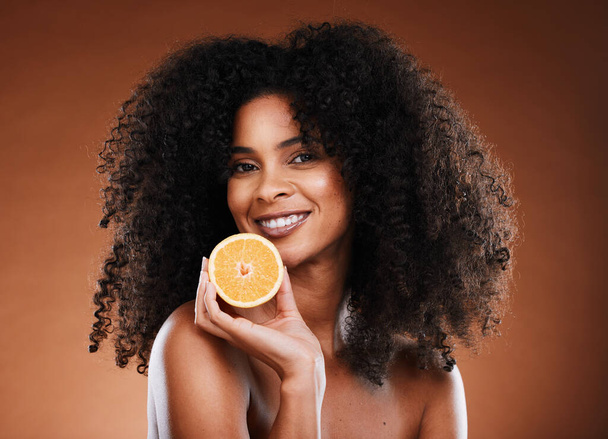 Orange, health and face of a black woman with fruit for skincare, nutrition and marketing against a brown studio background. Advertising, vitamin c and African model with food for nutrition and detox. - Foto, Imagem