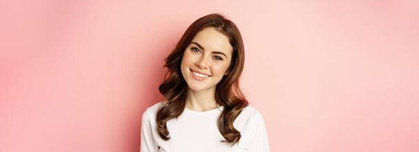 Close up of enthusiastic brunette girl with makeup, smiling and looking happy at camera, posing against pink background. - Φωτογραφία, εικόνα