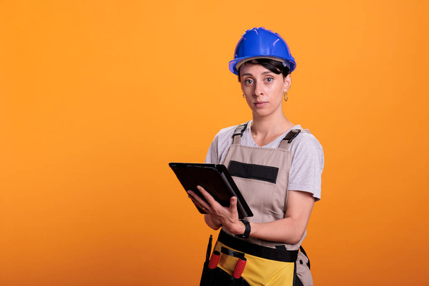 Portrait of woman builder working with digital tablet, looking for renovating inspiration online on wireless gadget. Female contractor in overalls using electronic digital device. - Fotografie, Obrázek