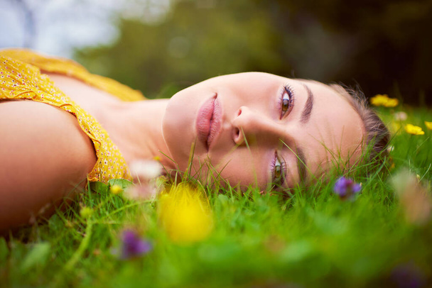 Bugün tek bir kuralım var, rahatla. Genç bir kadının portresi çimen ve çiçeklerle dolu bir tarlada yatıyor. - Fotoğraf, Görsel