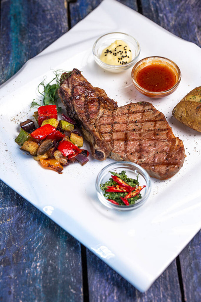 juicy fried steak with vegetables and sauce on a white plate on a blue wooden table. - Foto, immagini
