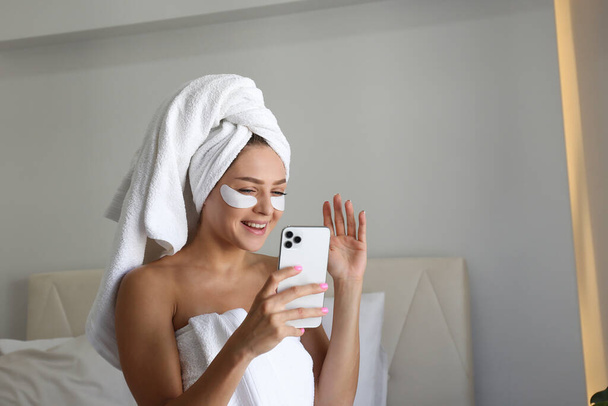 Young woman wearing a towel after showering recording a video review of the under eye patch for dark circles treatment for her beauty blog. Close up, copy space, background. - Foto, Imagen
