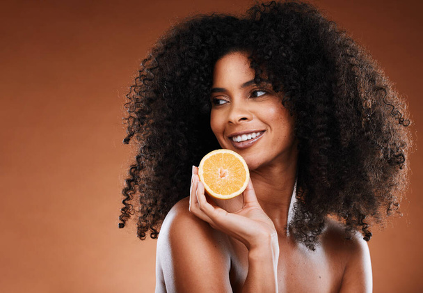 Black woman, fruit and natural beauty with an orange for skincare, health and glowing skin on a brown background. Cosmetic, vitamin c and citrus for organic facial treatment product and skin care. - Foto, Imagen