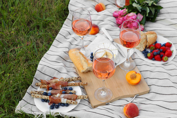 Glasses of delicious rose wine, flowers and food on picnic blanket outdoors - Photo, Image