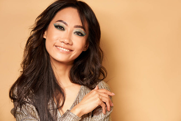 Smiling beautiful woman looking at camera with copy space. Happy asian girl model with long hair and bright makeup on beige background closeup - Fotoğraf, Görsel