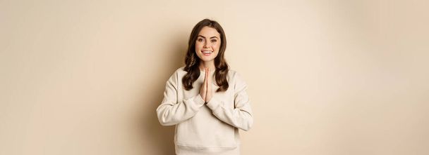 Thank you. Smiling happy woman showing pray, namaste gesture, thanking, standing pleased and grateful over beige background. - 写真・画像