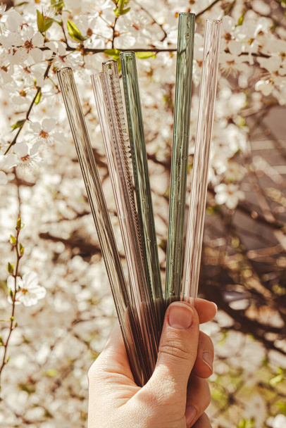 Herbruikbare glazen rietjes op de achtergrond van de natuur met groene bladeren lentebloemen Milieuvriendelijk Drinkstro Set Herbruikbaar Comfortabel Afgeronde punt. Geen afval, plastic vrij concept. Duurzame levensstijl - Foto, afbeelding