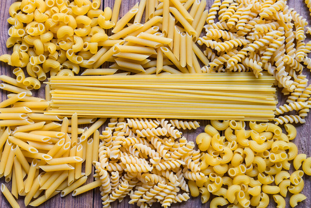Syrové těstoviny různé druhy tepelně neupravených špaget s makarony a nudlemi na dřevě - pohled shora, italský gastronomický koncept, Sbírka různých syrových těstovin na kuchyňském stole pro vaření potravin - Fotografie, Obrázek