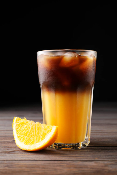 Tasty refreshing drink with coffee and orange juice on wooden table against dark background - Foto, afbeelding