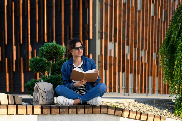 Young woman reading book on bench outdoors - Foto, imagen