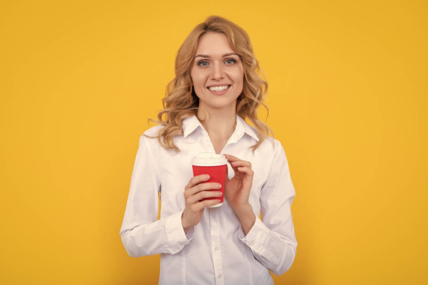 mujer rubia positiva con taza de café sobre fondo amarillo. - Foto, imagen