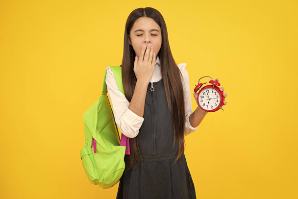 Back to school. Teenage school girl with bag hold clock alarm, time to learn. Schoolgirl on isolated yellow background. Tired and bored teenager girl - Foto, Imagen