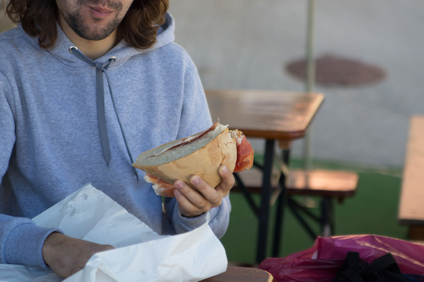jeune homme aux cheveux longs mange un gros sandwich
 - Photo, image