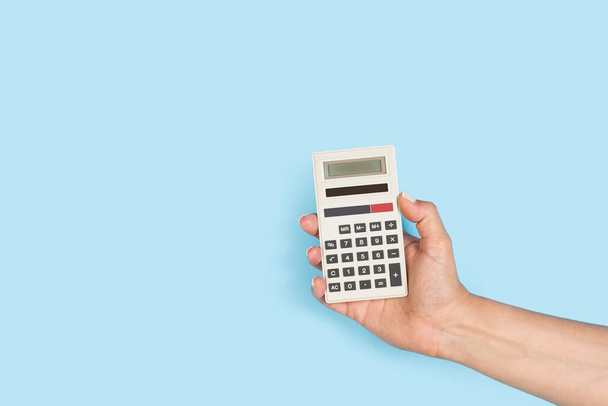 Woman hand holding a calculator floating on a light blue background with a copy space - Fotó, kép