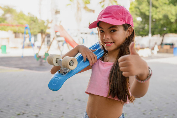 Χαρούμενο κοριτσάκι που κάνει σκέιτμπορντ στο πάρκο της πόλης. Ευτυχισμένο χαριτωμένο παιδί προσχολικής ηλικίας απολαύσετε και να διασκεδάσουν υπαίθρια τρόπο ζωής εξάσκηση extreme sport skating στις καλοκαιρινές διακοπές. - Φωτογραφία, εικόνα