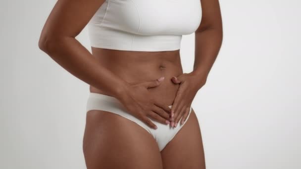 Schmerzhafte Phasen. Nahaufnahme einer nicht erkennbaren schwarzen Frau in Unterwäsche, die unter Bauchschmerzen leidet, den Bauch berührt, weißer Studiohintergrund, Zeitlupe - Filmmaterial, Video