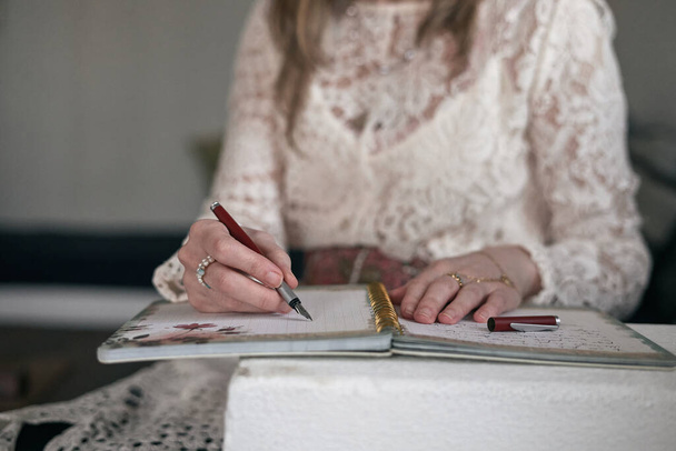 closeup of the hands of a caucasian mature woman with rings and a fountain pen in her right hand writing in a notebook - Adult artist - Photo, Image