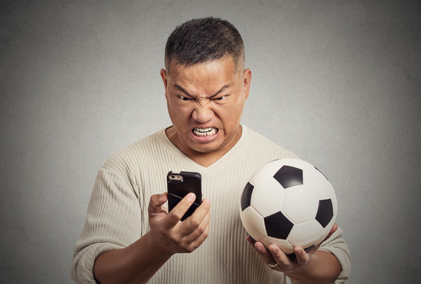 frustrated man looking on cell smart phone watching game holding football  - Foto, Imagen