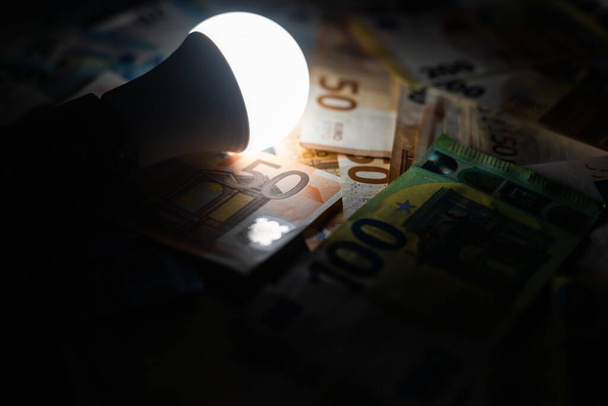 LED bulb on, with fluorescent bulb and incandescent bulb, with bills and coins next to it. Energy costs and evolution of light bulbs. - Photo, Image