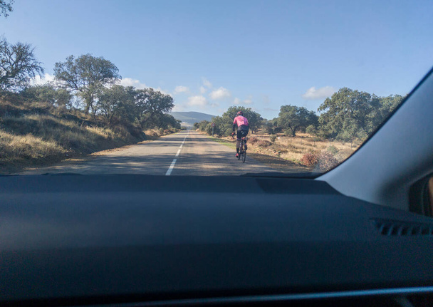 Медленно едет за велосипедистом по проселочной дороге. Вид изнутри автомобиля - Фото, изображение