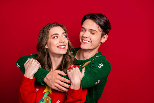 Photo of cheerful lovely couple wife husband wear ugly jumper hugs look each other enjoy cozy time isolated on red color background. - Photo, image