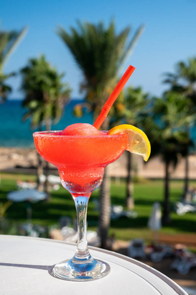 Bebida colorida de coquetel rosa congelada daiquiri de morango servida em vidro no bar da piscina com vista para a piscina azul, mar e palmeiras, relaxe e férias no mar - Foto, Imagem