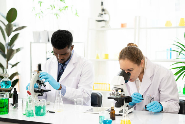 Ομάδα Μικροβιολόγων Κοιτάζοντας ένα δείγμα κρέατος φυτικής καλλιέργειας σε μικροσκόπιο. Ιατρικός επιστήμονας που δουλεύει πάνω σε φυτά. Εργαστήριο ιατρικής βιοτεχνολογίας με μικροσκόπιο. - Φωτογραφία, εικόνα