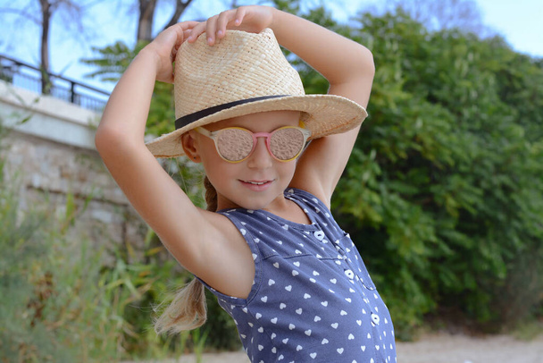 Little girl wearing sunglasses and hat at beach on sunny day - Fotó, kép