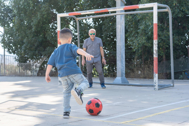 Takaisin näkymä lapsi potkii jalkapalloa. Isoisä jalkapallo maalivahti vartiointi jalkapallo tavoite. - Valokuva, kuva