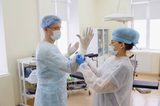 Cerrah ameliyata hazırlanıyor. Bir asistan deneyimli bir baş cerrahın steril lastik eldiven giymesine yardım eder. ilaç, ameliyat - Fotoğraf, Görsel