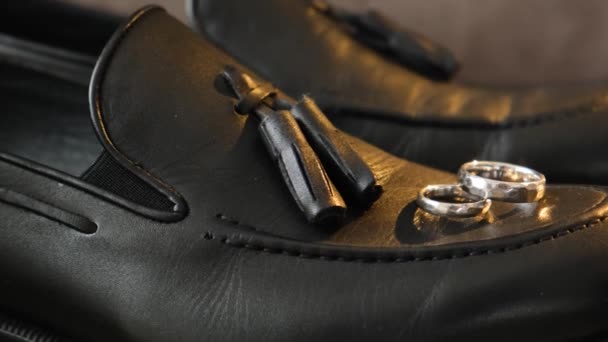Primer plano de los novios zapatos de cuero con anillos de boda de oro. Los novios accesorios de boda. La mañana antes de la boda - Metraje, vídeo