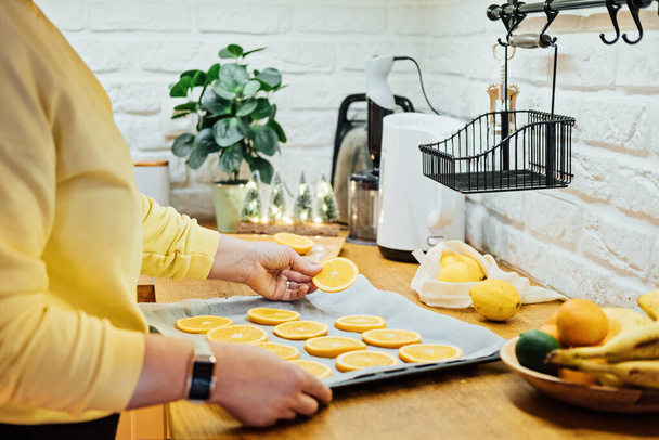How to Dry Orange Slices for Holiday Decor. Process of Drying Orange Slices in the Oven. Woman cutting slices of orange and citrus fruits for drying in oven in home kitchen. - Foto, Imagen
