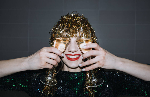 Gelukkig Nieuwjaar. Oudejaarsavond feest vieren. Mooie vrouw met vakantie make-up en goud glanzende folie pruik met glas champagne - Foto, afbeelding