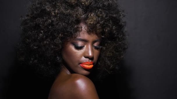 Mooi portret van een sensueel Afro-Amerikaans fashion model met blote schouders, kleurrijke make-up en afro haar geïsoleerd op zwarte achtergrond. - Video