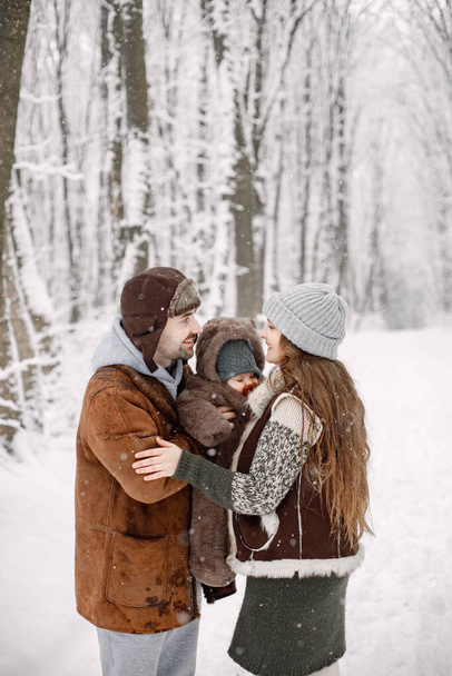 Parents with their baby son having fun in forest on snow day. Bearded man, brunette woman and baby son wearing warm clothes. Mother and father holding their son on hands. - Photo, Image