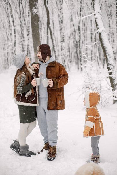 Parents with their toddler daughter having fun in forest on snow day. Bearded man, brunette woman and little girl wearing warm clothes. Mother and father hugging. - Foto, immagini