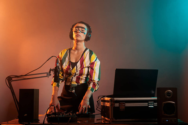 Cheerful musical artist working as dj with turntables, mixing techno music with bass and audio equipment. DJ woman playing songs at mixer, standing over colorful background with smoke. - Photo, image